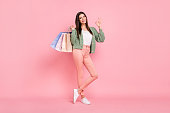 Full length photo of happy brunette young woman show okay sign smile hold bags isolated on pink color background