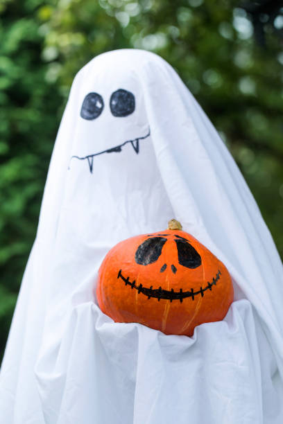 istock Ghost holds pumpkin with spooky face in green backyard 1338850297