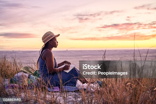 istock Shot of a young woman writing in her journal at the beach 1338851493