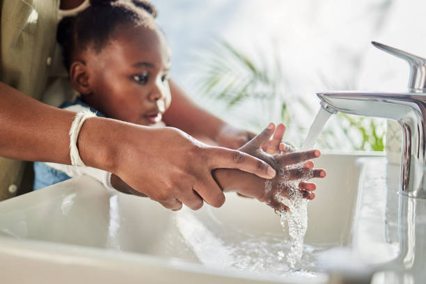 nahaufnahme einer mutter, die ihrer tochter hilft, ihre hände an einem wasserhahn in einem badezimmer zu hause zu waschen - freshness human hand mother family stock-fotos und bilder