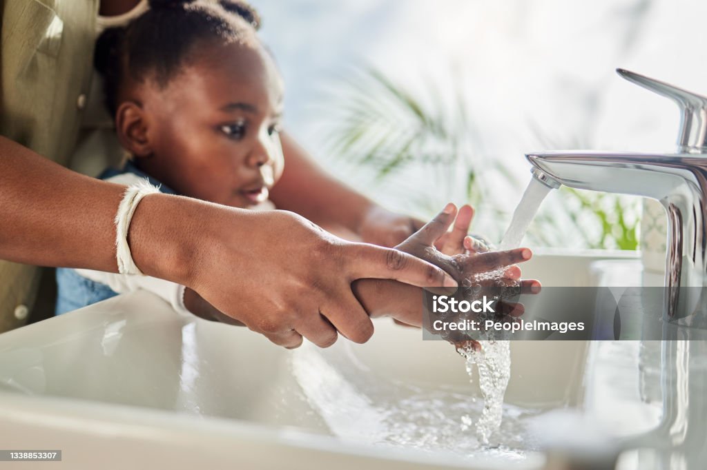 Closeup shot of a mother helping her daughter wash her hands at a tap in a bathroom at home Healthy habits help develop healthy lifestyles Faucet Stock Photo