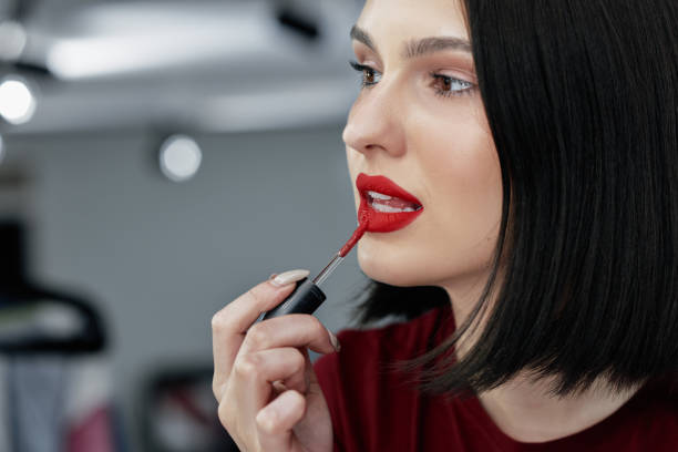 retrato sincero en primer plano de una joven atractiva que se aplica lápiz labial rojo. mujer morena con labios rojos haciendo maquillaje y un tutorial en línea con producto de belleza. - red lipstick fotografías e imágenes de stock