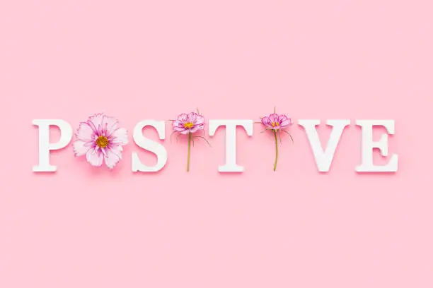 Photo of Positive. Motivational quote from white letters and beauty natural flowers on pink background. Creative concept inspirational quote of the day