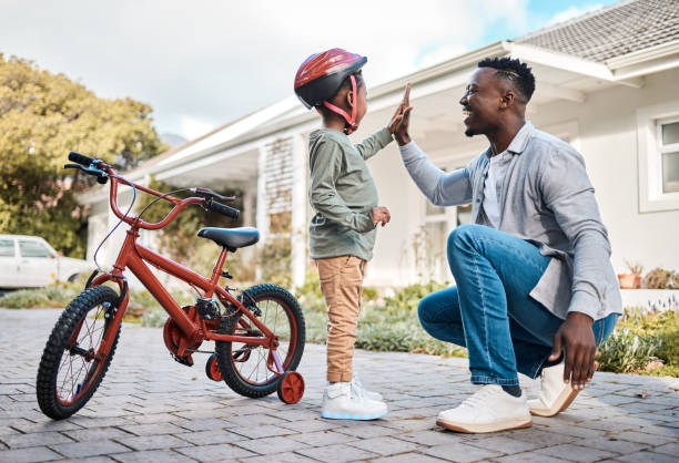 tiro de um pai e seu filho dando um ao outro um cinco alto enquanto andava de bicicleta ao ar livre - african descent cycling men bicycle - fotografias e filmes do acervo