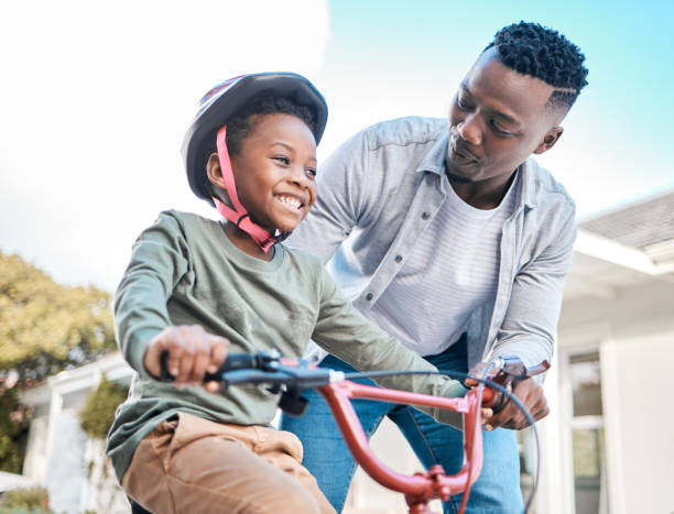 tiro de um pai ensinando seu filho a andar de bicicleta ao ar livre - african descent cycling men bicycle - fotografias e filmes do acervo