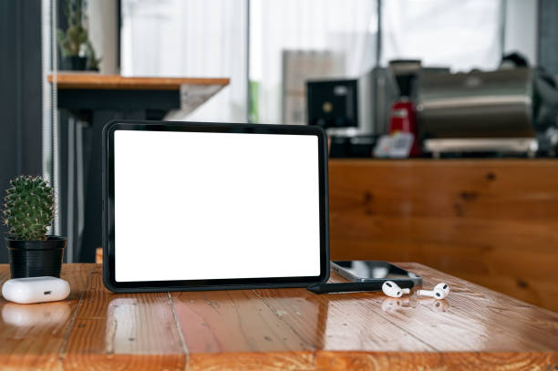 istock Blank white screen tablet with gadget on wooden table in cafe. 1338857551