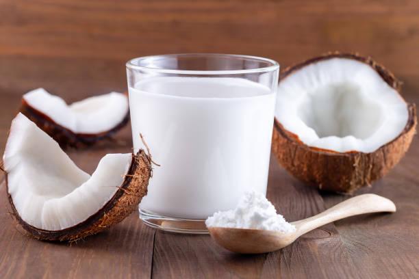 молоко без лактозы. кокосовое молоко в сухом виде и растворенное водой в стакане на деревянном фоне, вертикальном - powdered coconut стоковые фото и изображения