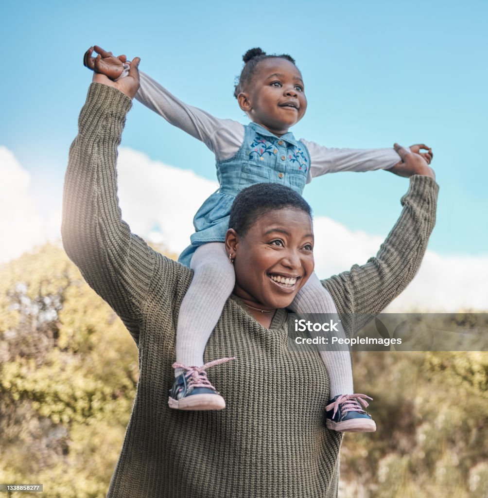 Shot of a mother carrying her daughter on her shoulders outdoors It's all smiles when they're at the park Child Stock Photo