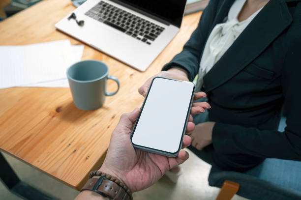 istock Closeup image of man hand passing mobile with blank screen to his partnership while working in office. 1338859063