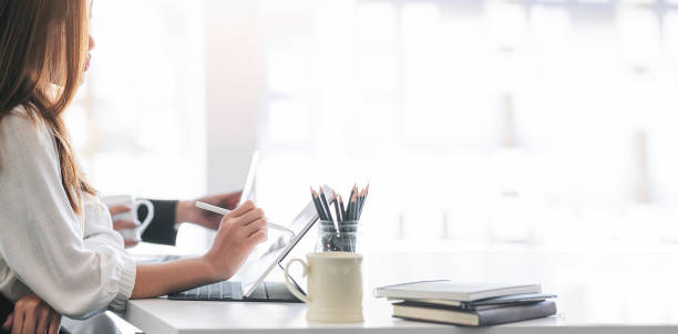 istock young woman using stylus pen working on tablet while sitting in modern office. 1338859121