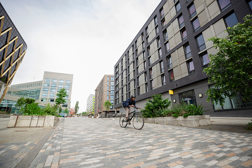 A mature black man wearing formal businesswear and a helmet on a summers day in a city. He is riding bicycle as he sustainably commutes to work.