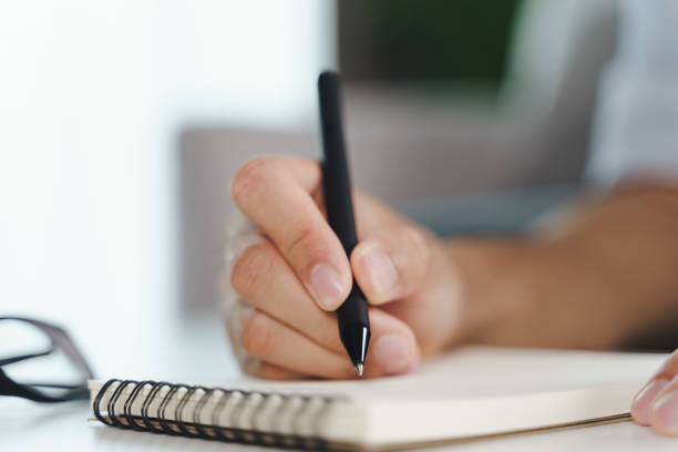 istock Close up of young man in casual cloth hands writing down on the notepad, notebook using ballpoint pen on the table. 1338864368