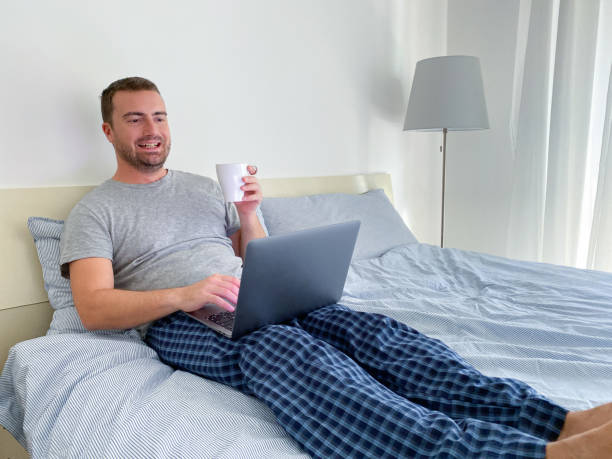 istock Man lying in bed with his laptop and working from home 1338864831