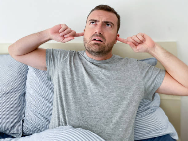 retrato de un hombre enojado en la cama molesto por el ruido - hand to ear fotografías e imágenes de stock