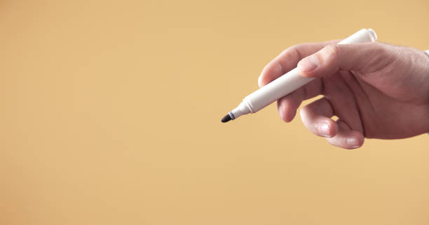 istock Male hand holding a marker isolated on yellow background. 1338875977