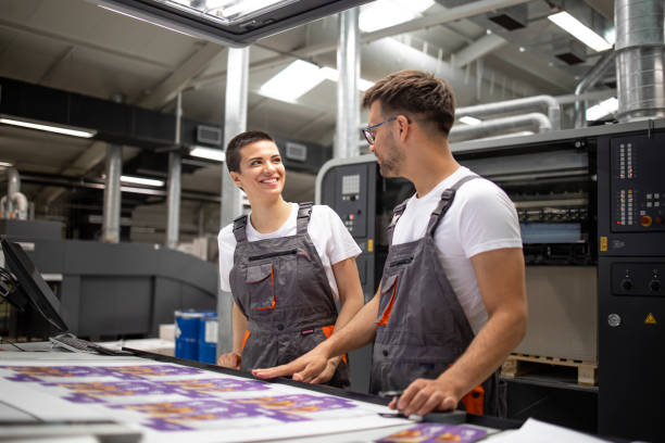 istock Printing machine operators checking graphic quality and color values at print shop. 1338879093
