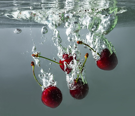 ripe cherries fall into the water raising splashes and air bubbles