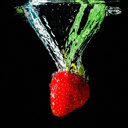 ripe strawberries fall into the water lifting splashes and air bubbles