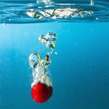 ripe cherries fall into the water raising splashes and air bubbles