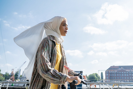 retrato de una joven con hiyab en un patinete eléctrico en riverside en Berlín photo