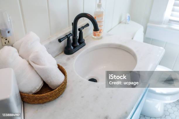 A Basket Of Organized Clean Rolled White Towels On A Bathroom Counter In A Guest Bathroom Near A Sink And Toilet Stock Photo - Download Image Now