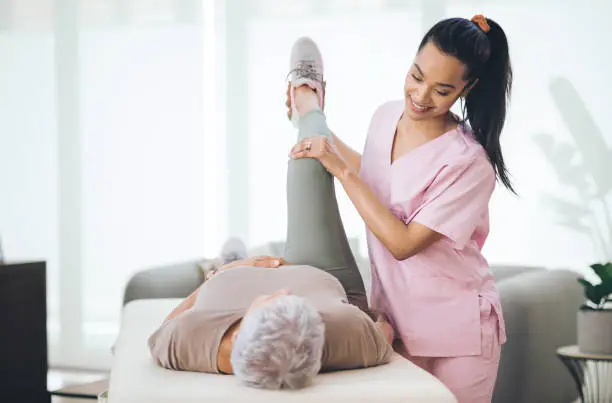 Photo of Shot of an older woman doing light exercises during a session with a physiotherapist inside