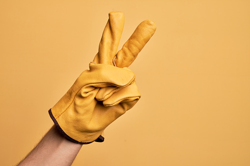 Hand of caucasian young man with gardener glove over isolated yellow background counting number 2 showing two fingers, gesturing victory and winner symbol