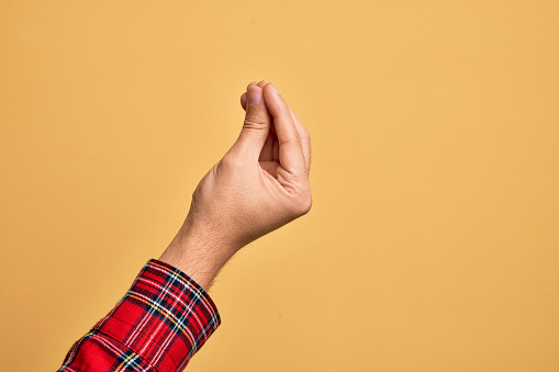 Mano de un joven caucásico que muestra los dedos sobre un fondo amarillo aislado haciendo gestos italianos con los dedos juntos, movimiento de gestos de comunicación photo