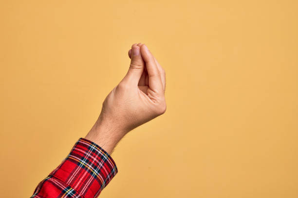 р�ука кавказского юноши показывает пальцы над изолированным желтым фоном, делая итальянский жест пальцами вместе, движение жестов общения - italian culture стоковые фото и изображения