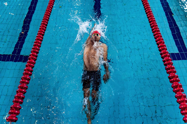 istock Young professional male swimmer in red cap and goggles practicing and training at pool, indoors. Healthy lifestyle, power, energy, sports movement concept 1338889235