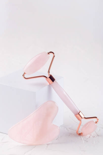 Rose quartz crystal facial roller and massage tool Gua sha on white background, vertical, copy space