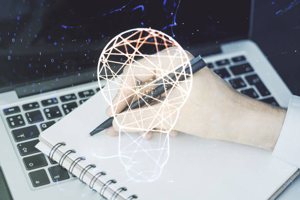 istock Creative light bulb hologram with hand writing in notepad on background with laptop, idea concept. Multiexposure 1338891299
