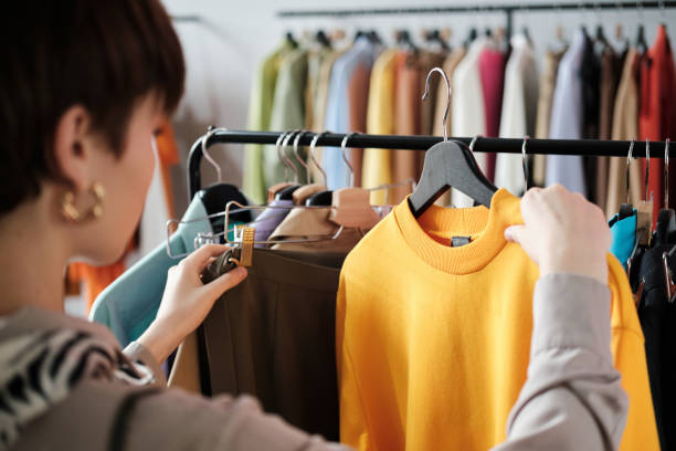 Woman choosing a new style for herself Rear view of young woman looking at clothes on rack in her hands and choosing a new style for herself in the clothes store clothes shop stock pictures, royalty-free photos & images
