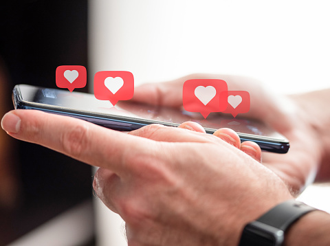 person getting likes on social media, close-up of hands holding smartphone with heart icons hovering above