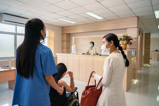 Nurse service pushing asian patient woman on wheelchair to contact the receptionist to admitted in the hospital