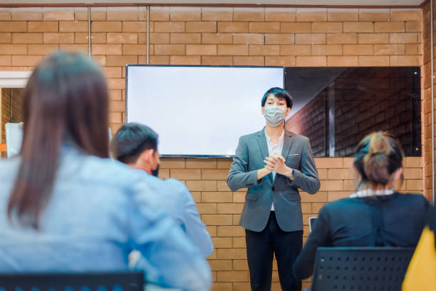 istock business cooperation : Young asian male coach or speaker make flip chart presentation to diverse businesspeople at meeting in office. Male tutor or trainer present project to diverse colleagues. 1338898681