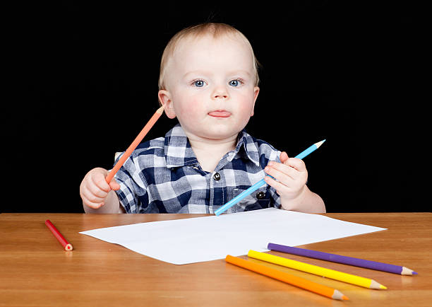 Young boy sitting at desk with pencils drawing stock photo