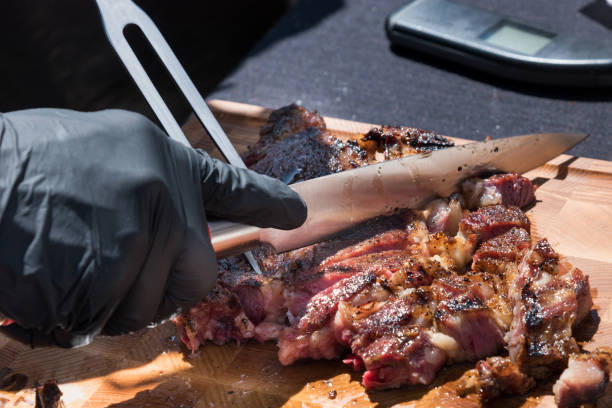 Chef carving a portion of grilled rib eye meat Gloved hand of a chef carving a portion of grilled prime rib eye meat from the BBQ on a wooden chopping board in a close up on the food barbecue beef stock pictures, royalty-free photos & images