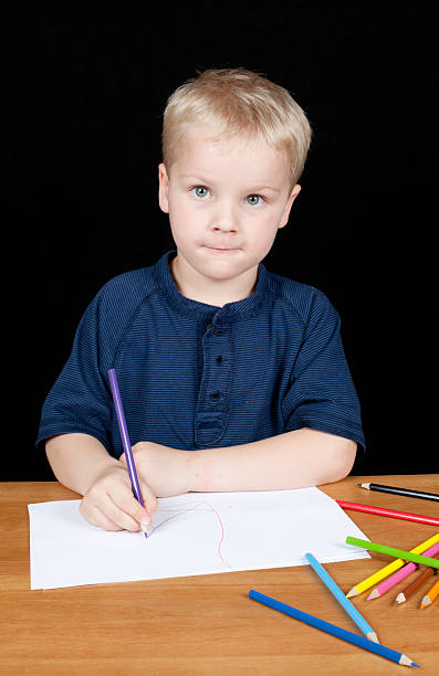 Young boy sitting at desk drawing a picture stock photo