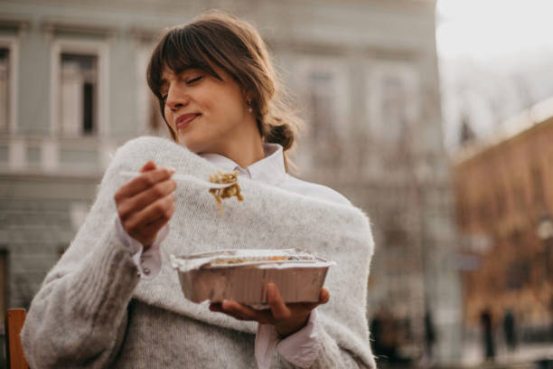 Love is in the air when eat Spontaneous and loving young adult woman, a brunette with bangs, elegantly dressed, sitting outdoors, on a beautiful autumn sunny day, eating her take out food with a big enjoyment. Radiating happiness and love fringe stock pictures, royalty-free photos & images