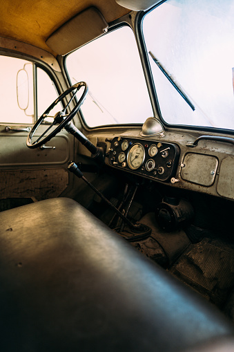 Interior of aged fire truck with steering wheel and speedometer with arrows above large leather seat in front of windshield with wipers and side mirror. Old vehicles concept