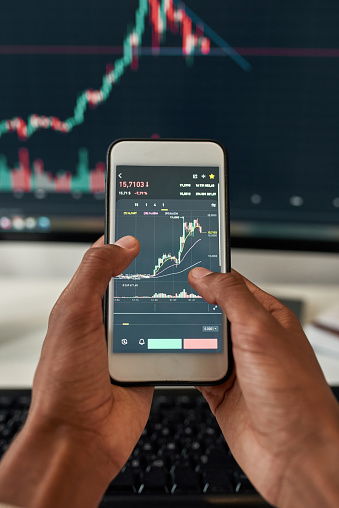 Close up top view of ethnic male trader use smartphone computer check financial graph chart money balance. Man investor exert trace online on stock market exchange. Cryptocurrency concept. Depicts TradingView financial market chart.