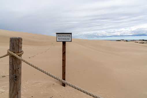 Wooden fence post and rope with a a no trespassing sign in the pristine sand dunes nature reserve of Slowinski Naitonal Park written in Polish and English