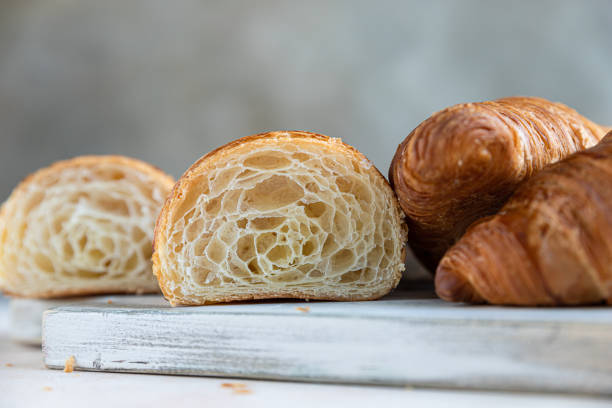 istock Cut in half croissant with inside texture and thin crisp layers on wooden board, light concrete background. Delicious french pastry. 1338909199