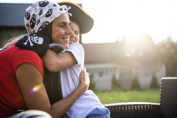 A cute boy and his mom are hugging while playing make-believe pretending to be pirates in their yard
