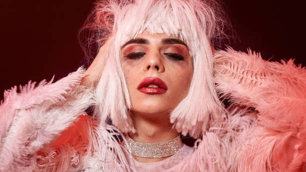 istock Sensual drag queen, young transgender with rubbed bright night makeup wearing boa feather party dress and white wig, posing isolated in red neon light background 1338911917