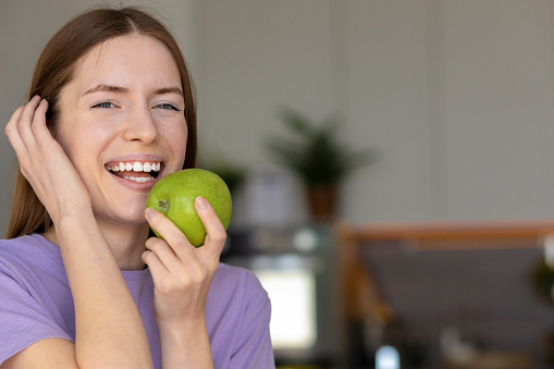 Beautiful caucasian woman with white teeth smiling and eating a green apple, healthy lifestyle