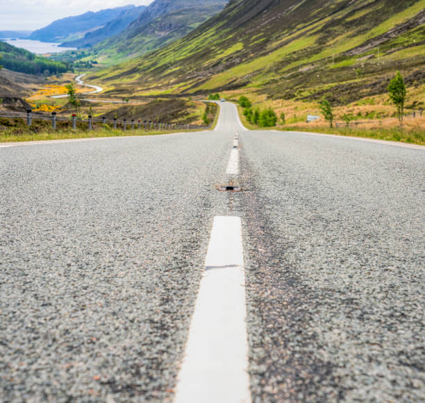 A winding road on Scotland's famous North Coast 500 driving route, with Loch Maree on the horizon in the North West of Scotland.
