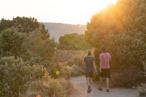 In Black Canyon of the Gunnison National Park in Colorado, United States two people walk along a hiking trail towards the setting sun in summer.