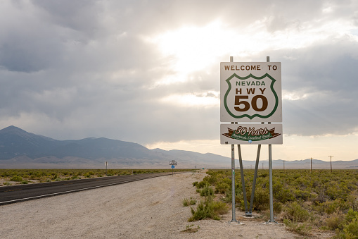 In Baker, United States a Welcome to Nevada Highway 50 sign is posted next to a rural road in the desert.